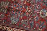 Close-up of vintage Mahal carpet's worn brick red field, colorful floral motifs, exposed foundation.