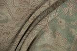 Distressed Oushak rug pile, folded with muted sea foam green and pale coffee brown tones.