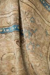 Folded vintage Tabriz carpet with distressed beige pile and faded sky blue motifs.