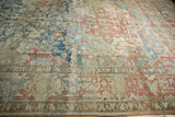 Textured, distressed vintage Heriz carpet showcasing faded blue, red, and neutral floral motifs with border.