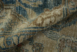 Folded vintage Heriz carpet, distressed pile, with beige, blue, and brown floral pattern detail.