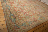 Distressed traditional Mahal carpet corner, featuring faded terracotta and blue floral motifs.