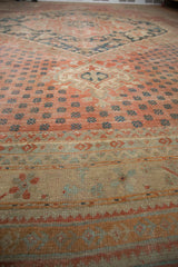 Distressed vintage Oushak rug with a soft, worn texture showing muted raspberry field, small blue motifs, and patterned sand-colored borders.