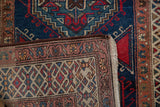 Folded corner of vintage Persian runner reveals tight geometric back and deep navy, red pile.