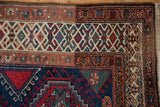 Vintage Northwest Persian rug corner, showing navy field, red guls, and layered geometric borders.