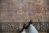 The worn, low-pile texture of a vintage Tabriz rug, showing the ornate navy border for scale.