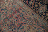 The distressed weave of a vintage Persian rug, highlighting blush tendrils beside a dark navy border.