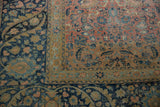 A distressed Tabriz rug corner with an intricate navy floral border and a worn blush-toned field.