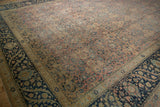 Angled view of a vintage Tabriz carpet's distressed blush field and wide dark navy floral border.