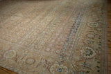Angled view of a distressed Tabriz carpet showing even wear across the sand-colored Herati field and navy border.