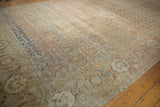 Angled view of a distressed Tabriz carpet highlighting the worn texture, navy inner border, and sand-colored field.