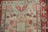 Geometric starburst motifs in red and sage against a worn pile showing visible knot heads.