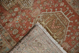 Corner detail of distressed vintage Heriz rug, showing worn reddish pile, fringe, and hand-knotted foundation.