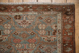 Distressed Hamadan runner corner: dusty blue, wine red pattern, worn pile texture, fringed edge.