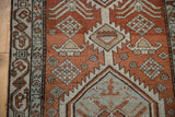 Distressed brick red field with even wear, pale blue geometric border, and small plant motifs.