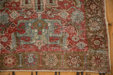 Distressed cherry red field with wear, bronze floral border, and short fringe on the Heriz runner.