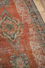 Close-up of distressed vintage Mahal rug, showing worn brick red pile and Rococo floral motifs.
