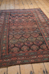 Secured end of vintage Kurdish rug with fringe, showing madder root red field and vine border.