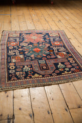 Fringed corner of the vintage Caucasian rug showing navy, purple, and tangerine finned animal motifs.