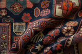 Folded vintage Caucasian rug detail with navy blue, purple, and tangerine geometric motifs.
