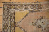 Distressed Oushak rug corner detail, highlighting starburst border, pale pink, saffron, and silver.