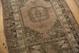 Angled view of distressed vintage Oushak rug showcasing muted beige and charcoal patterns.