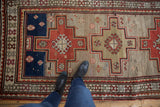 Geometric stepped medallions in red, blue, and silver on a vintage Caucasian runner's worn, low pile.