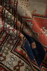 Textured, hand-knotted pile of a folded Caucasian rug showing the geometric crab-style border in red and navy.