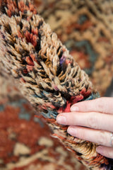 Hand touches the thick, plush pile of a vintage Tulu rug with varied abrash colors.