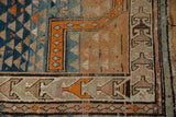 Vintage Caucasian rug detail: tangerine geometric borders, triangular motifs, and stylized sand patterns.
