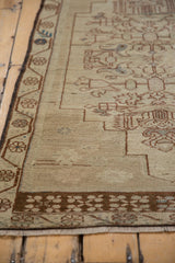 Distressed texture of the Oushak rug's ivory field and brown vine border with blue accents.