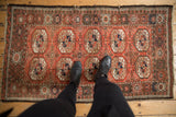 Feet on vintage Afghani Bokhara rug, highlighting madder red and brown gul motifs.