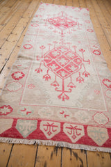 Distressed Oushak rug with cherry red diamond medallion, floral buds, and faded ivory tones.