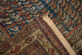 Folded corner of vintage Caucasian rug, showing its foundation and blue ground with rainbow fish motifs.