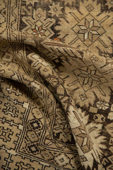 Folded Caucasian rug texture, revealing geometric starbursts in beige, charcoal, and orange.