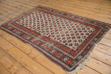 Vintage Caucasian rug shows geometric splayed floral and boteh pattern in ivory and wine red.