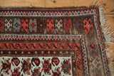 Vintage Caucasian rug corner: geometric borders, curvilinear design, worn ivory field, tattered fringe.
