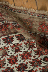 Aged fringe and reciprocating geometric pattern of vintage Caucasian rug in ivory, wine red, charcoal.