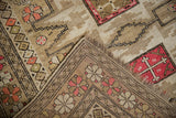 Folded corner of Caucasian rug: beige stepped geometric patterns, fringe, and red cross motif.