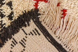 Textural view of a vintage Moroccan carpet's plush ivory pile, charcoal geometric motifs, and thick fringe.