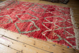 Angled view of a vintage Moroccan carpet's shaggy, abrashed red pile and diamond motif.