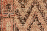 Moroccan carpet pile exhibiting high and low texture, rustic orange, ivory, and dark brown motifs.