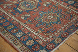 Vintage Karaja rug corner displaying geometric pawn motifs and floral border in brick red and indigo.