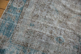 Corner view of a distressed Oushak rug with a worn pile in silver, brown, and dusty turquoise.