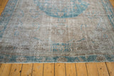 Corner of a distressed Oushak showing its secured selvage and time-softened pile in silver and dusty turquoise.
