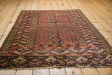 Low angle view across an antique Turkmen Hatchli rug, showing the depth of its geometric patterns in red and navy.