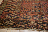 Corner detail of an antique Turkmen rug showing intricate, serrated geometric motifs in red and navy.