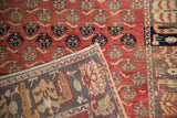 Folded corner of a distressed Oushak runner reveals the hand-knotted back against the red floral pile.