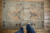 Distressed vintage Oushak rug with central finned floral medallion in beige, faded blue, and brown.
