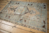 Distressed Oushak rug corner with worn pile, faded blue, beige, and brown tones.